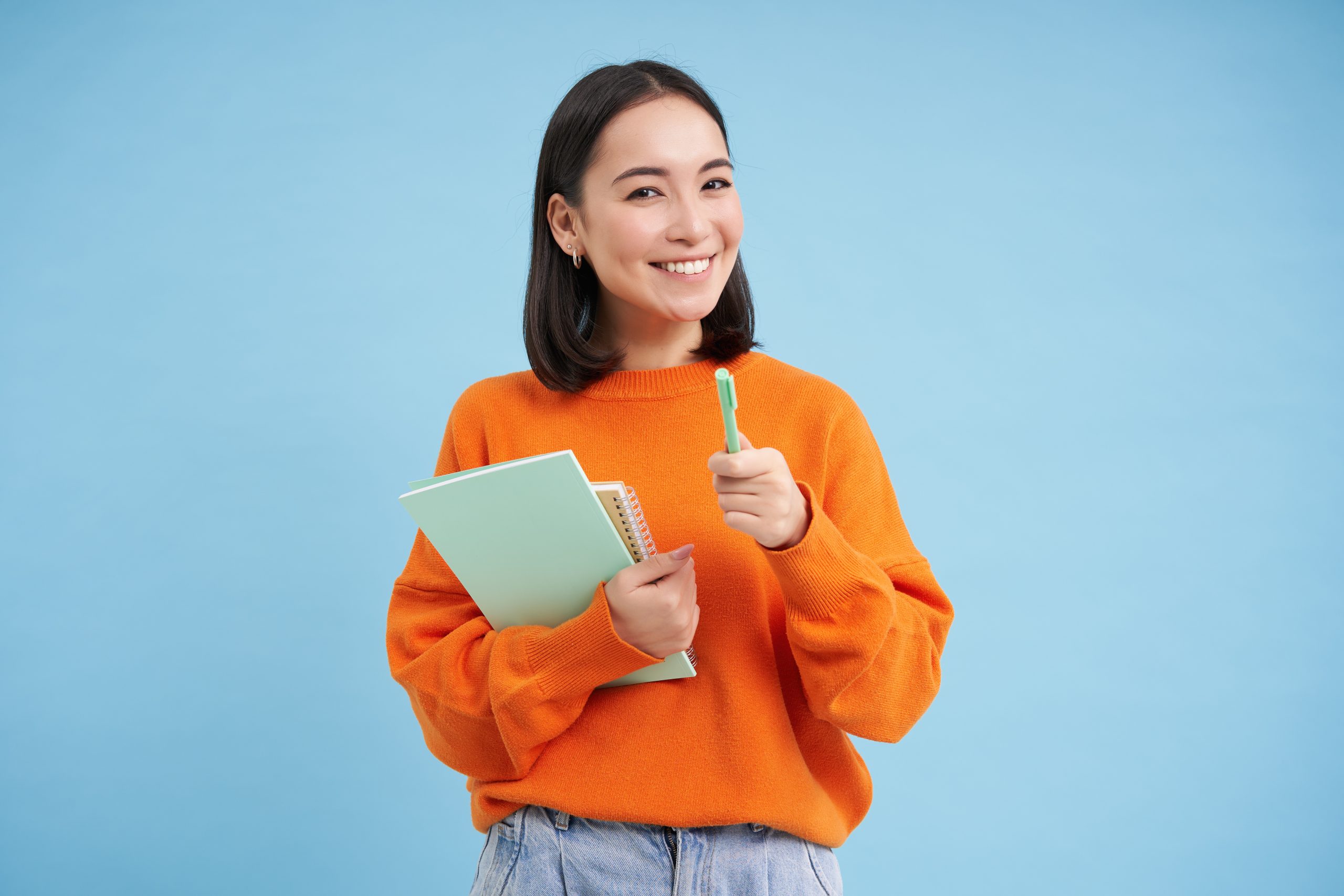 Education and students. Happy asian woman, holding notebooks and laughing, smiling at camera, enjoys going to University or College, blue background