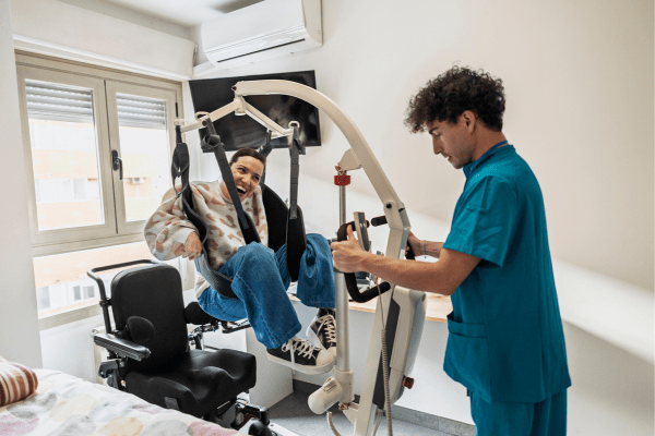 aide à la personne aidant une personne en situation de handicap à monter sur son fauteuil roulant